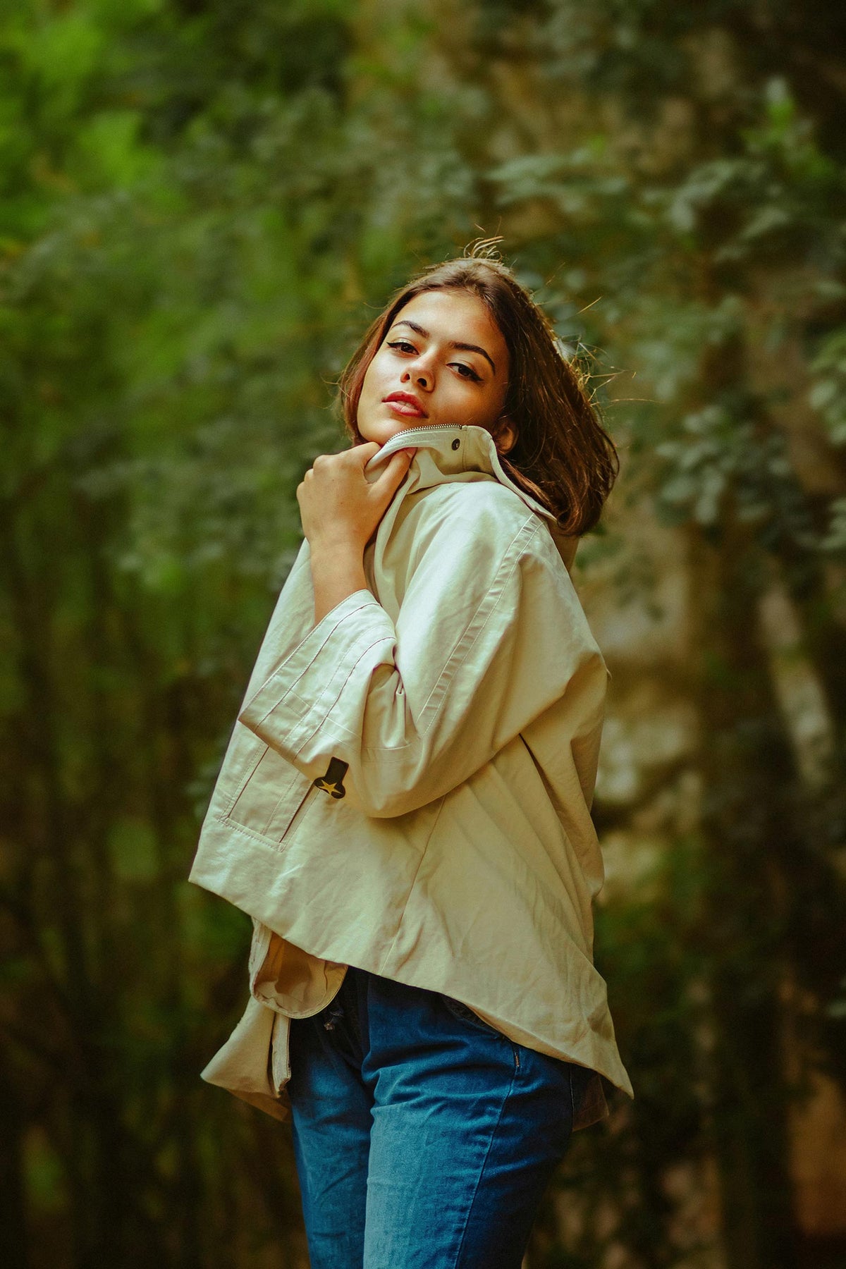 Woman wearing a beige jacket and blue jeans standing in a forest.Shoot with the telephoto lens of the APEXEL TeleMacro Pro 10X mobile phone