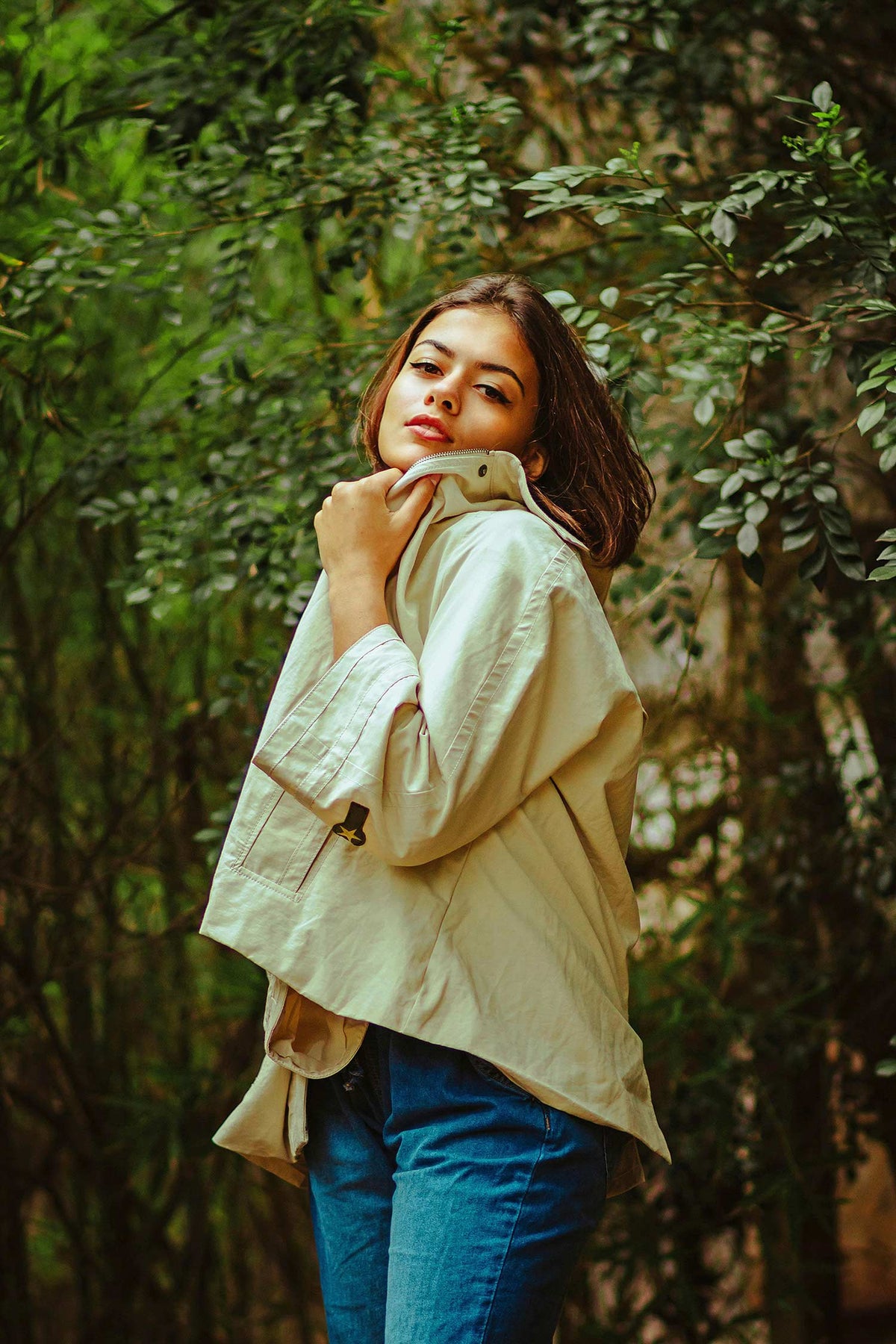 Woman in a beige jacket and blue jeans standing in a forest.Use the telephoto lenses of other 10X phones