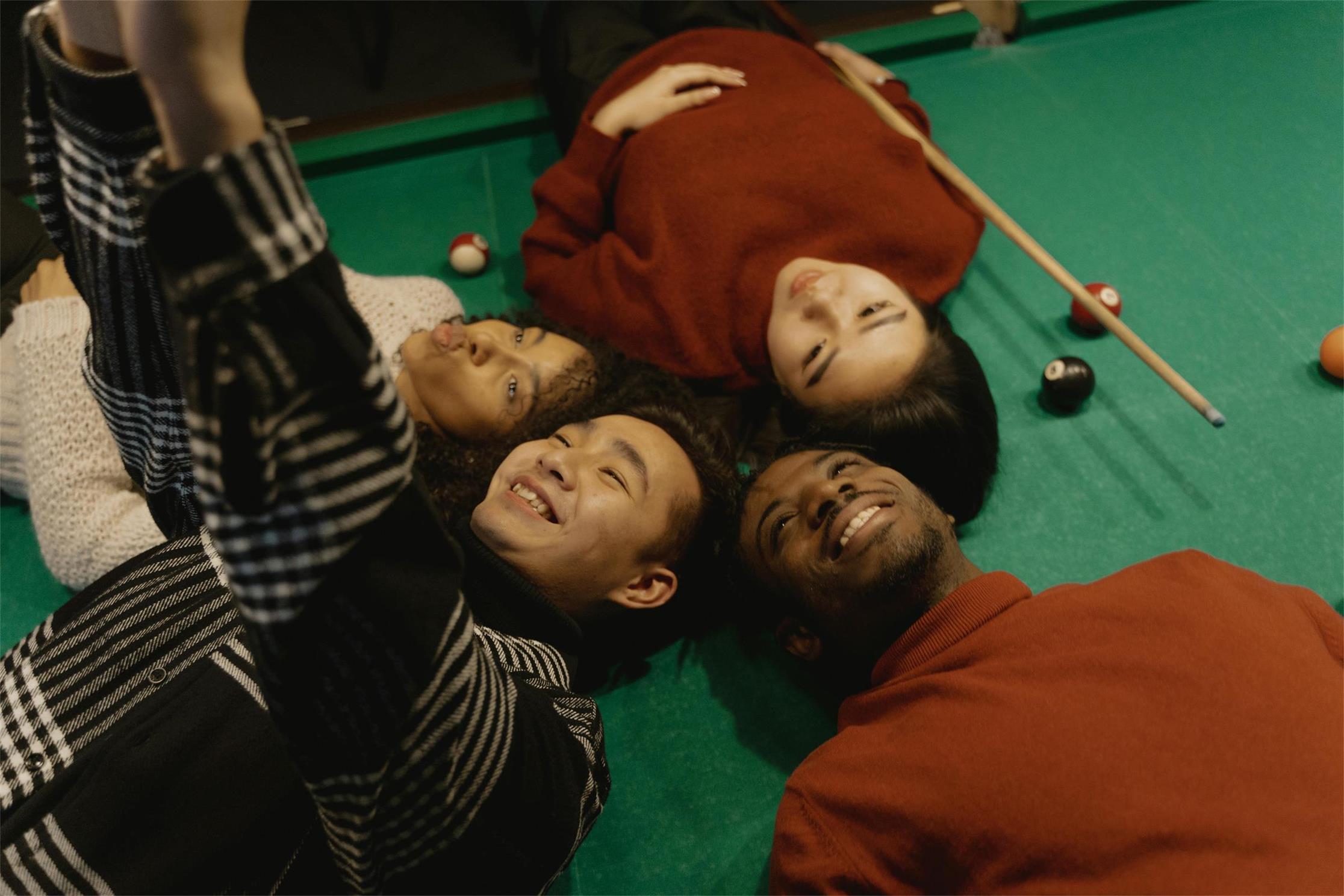 Three friends capturing a fun moment on a pool table, smiling and posing for a selfie. Enjoying the Apexel customer experience! 