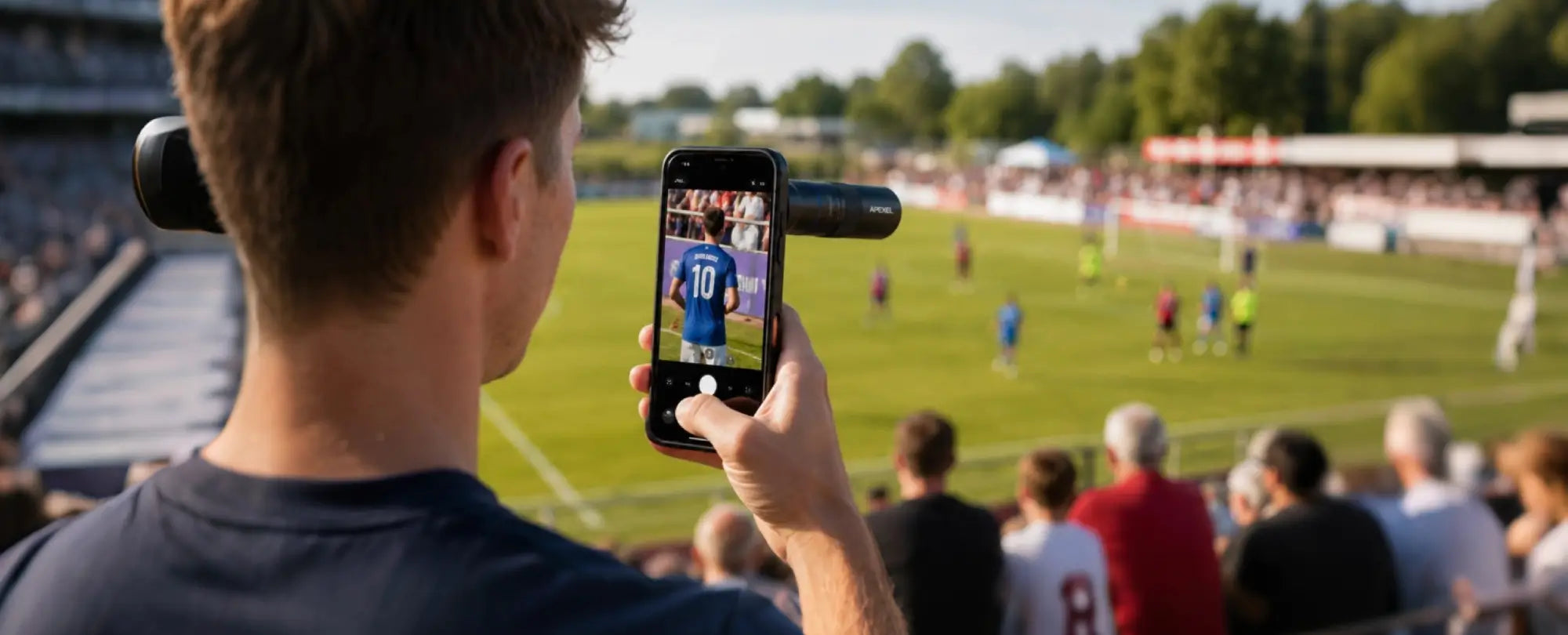 A man records a football match inside a stadium using an Apexel telephoto lens designed for smartphones.