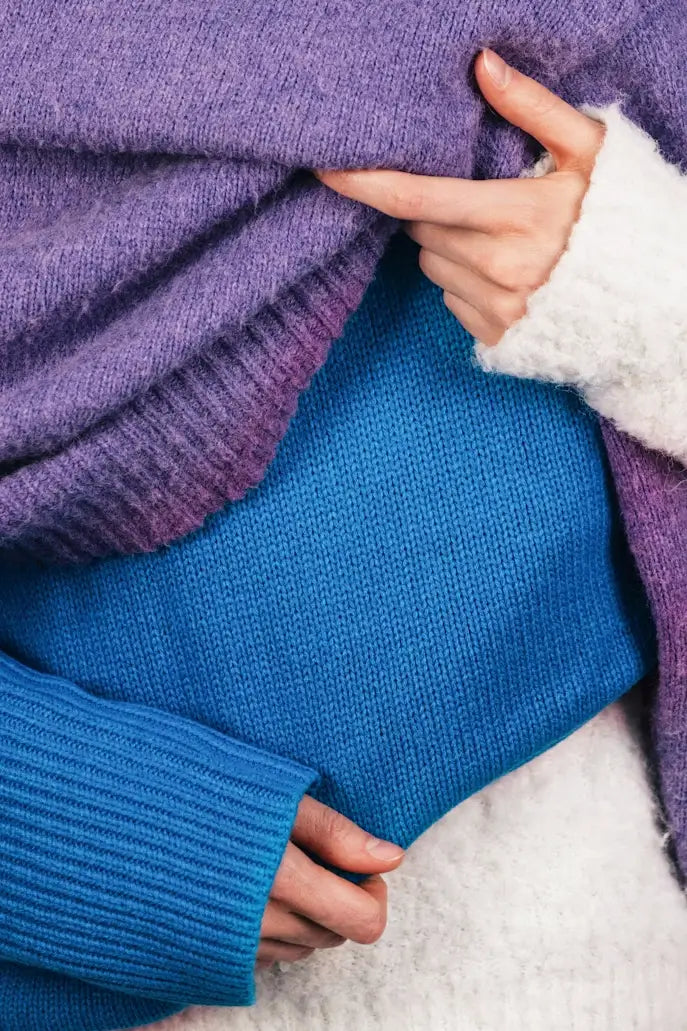 Close-up of hands holding a purple and blue sweater with white cuffs. Shot on iPhone 13 Pro Max